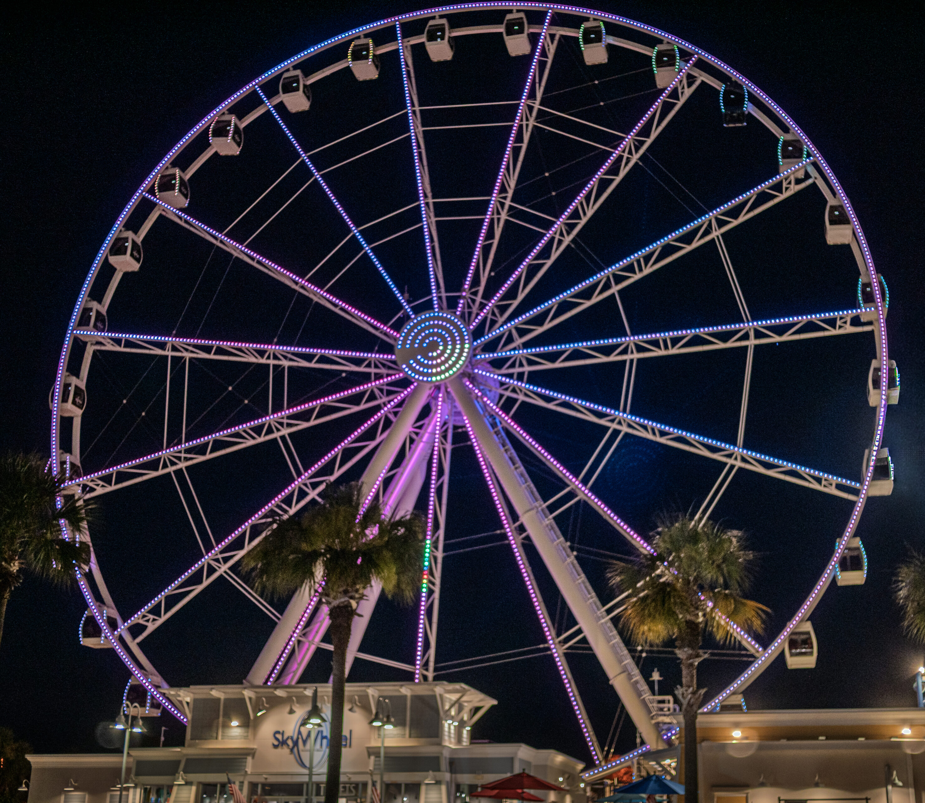 The brightly lit PCB wheel glowing with purple and blue neon lights against the night sky at Pier Park in Panama City Beach, Florida.
