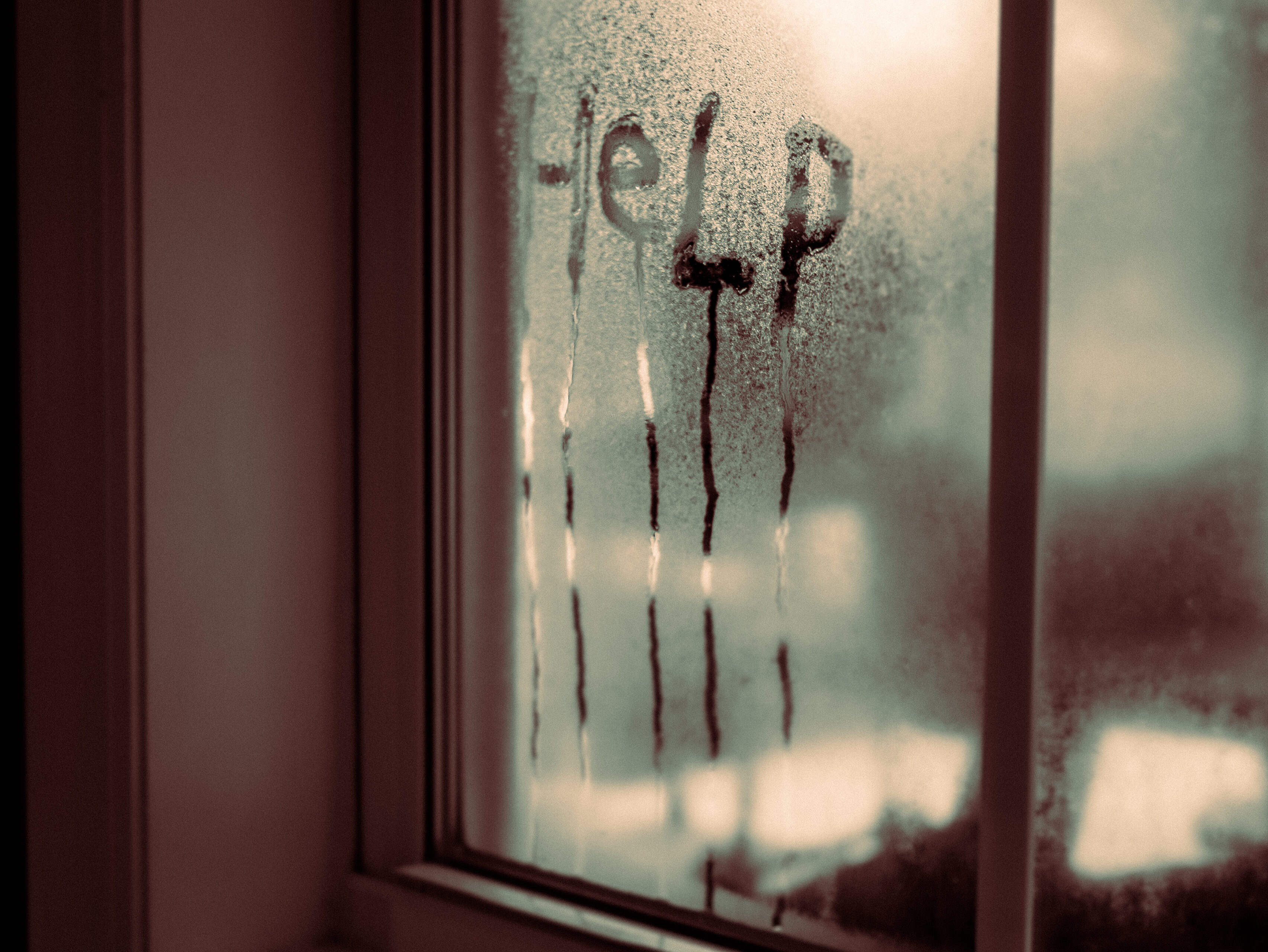 A fogged window with the word ‘Help’ written in condensation, water streaks running down the glass like tear marks, creating a haunting, cinematic atmosphere.